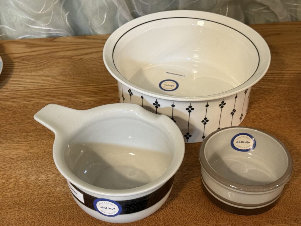 Three vintage bowls with different designs on a wooden table. In the back is a large white bowl with a black pattern, and in the foreground are a spouted bowl and a small bowl with gray stripes.