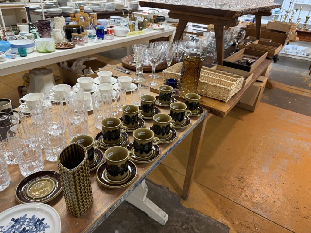 The interior of a second-hand shop in Helsinki. Vintage Arabia cups and saucers and Iittala glasses are arranged on wooden tables.