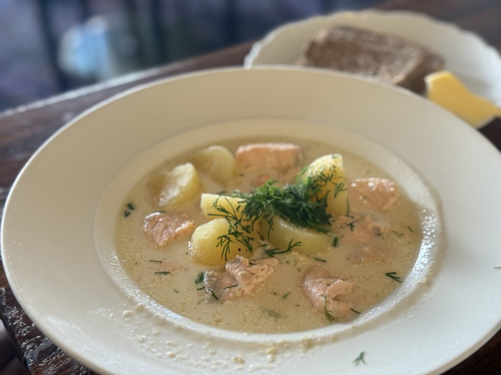 A creamy soup with large chunks of salmon and potato in a white bowl, garnished with fresh dill in the center.
