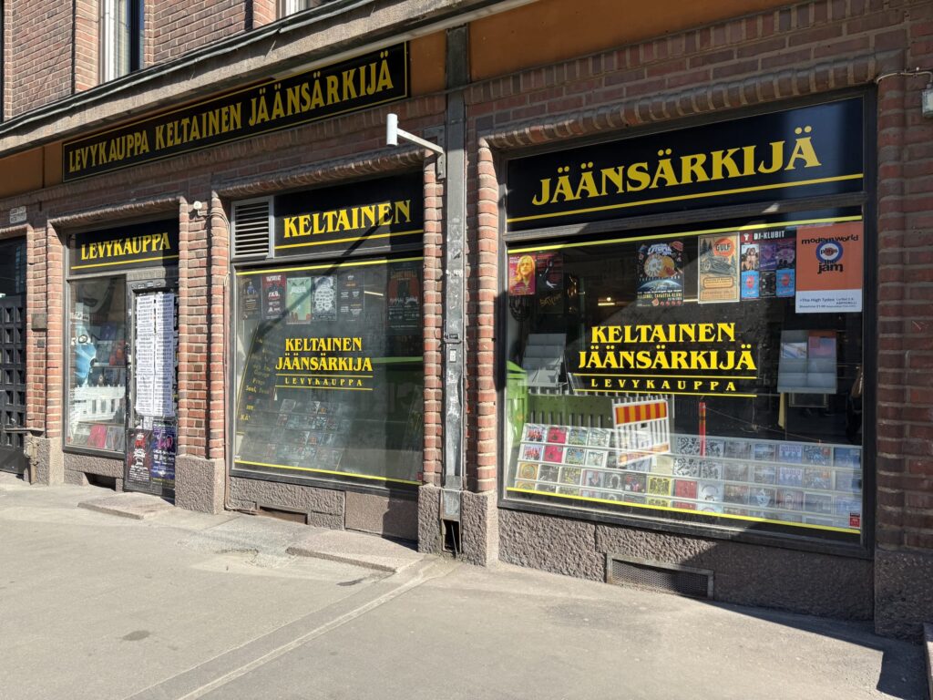 The brick exterior of the record store 'Levykauppa Keltainen Jäänsärkijä' in Helsinki, Finland. The show windows are decorated with records and posters.