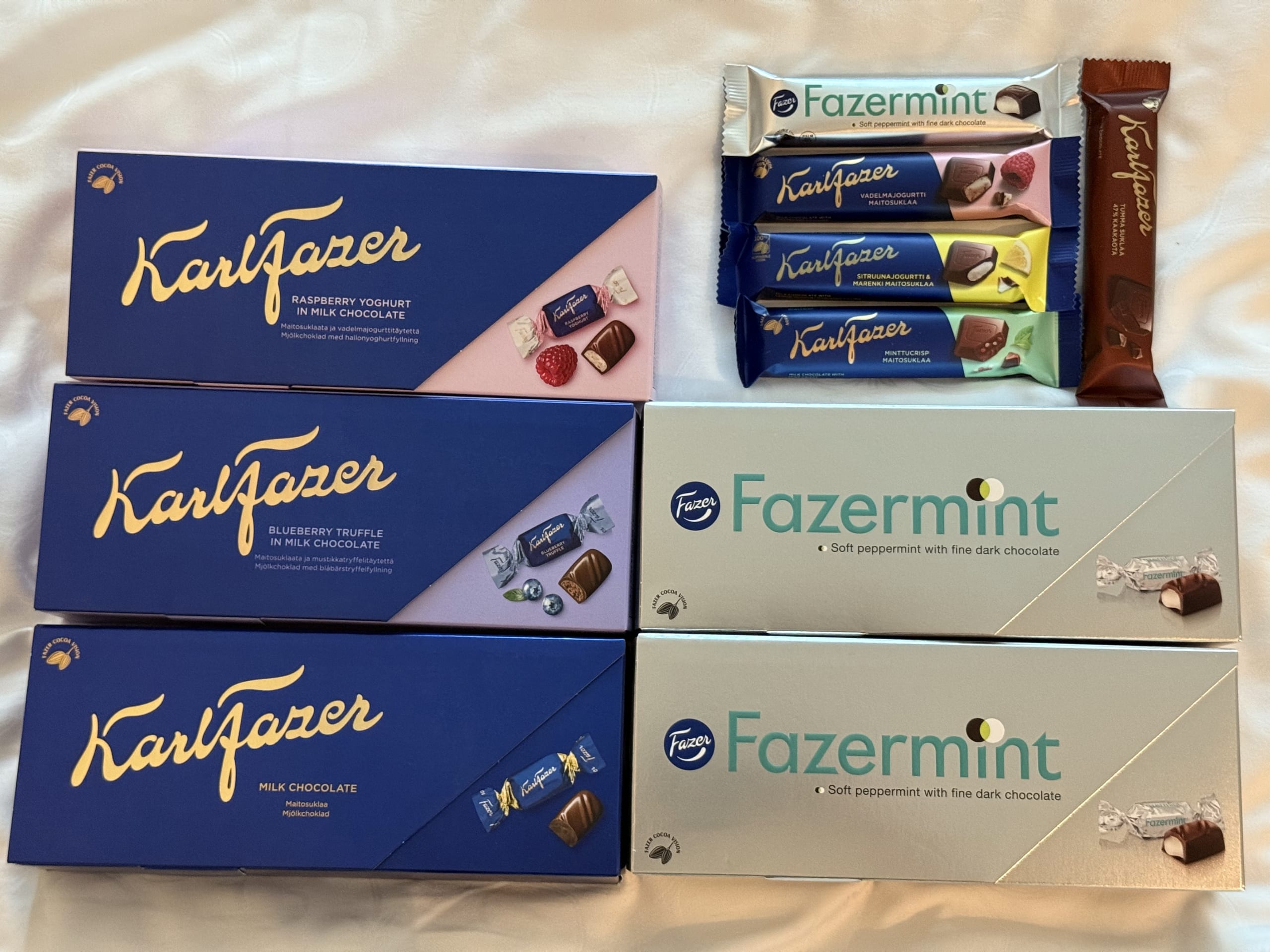 フィンランドのチョコレートブランド、ファッツェルのカール・ファッツェルとファッツェルミントのチョコレートボックスとチョコレートバー。ラズベリーヨーグルト、ブルーベリートリュフ、ミントなど様々なフレーバーが白い布の上に並べられている。
