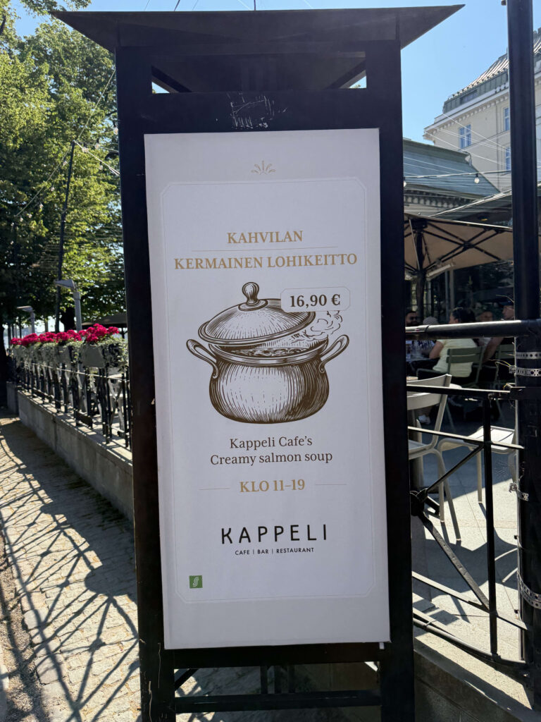 ヘルシンキのレストラン「カッペリ」の店先に置かれた、名物のクリーミーサーモンスープを宣伝する看板。スープのイラストと価格、提供時間が書かれている。