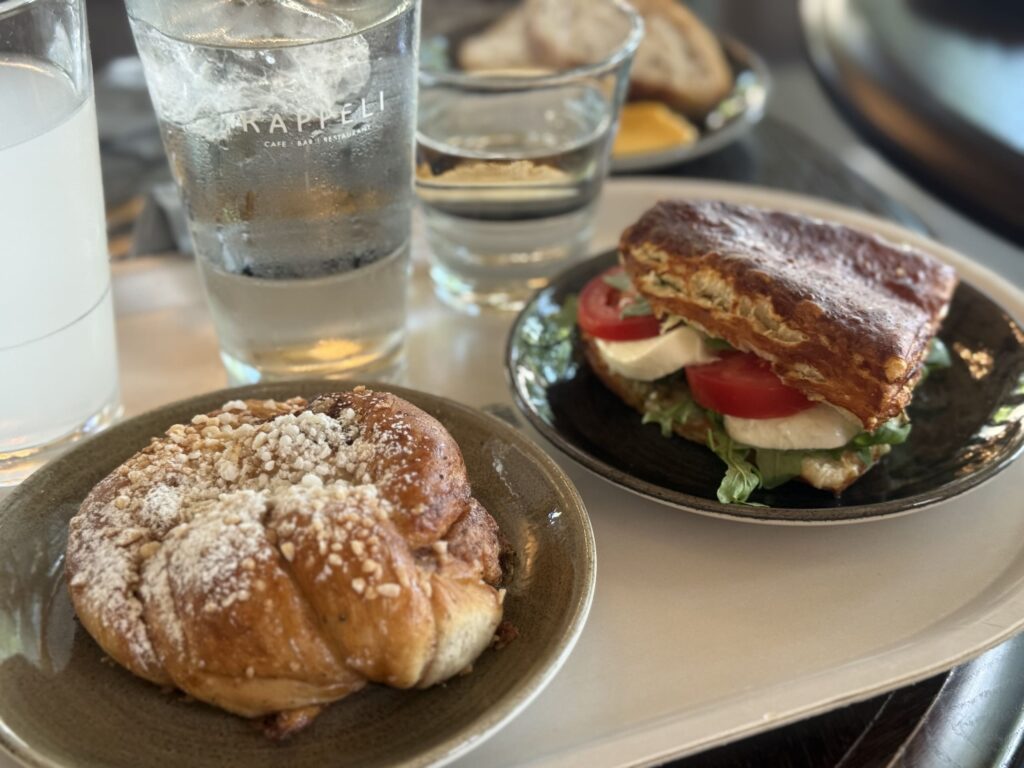 カフェのトレイにのったシナモンロールとカプレーゼサンド、そして水の入ったグラス。