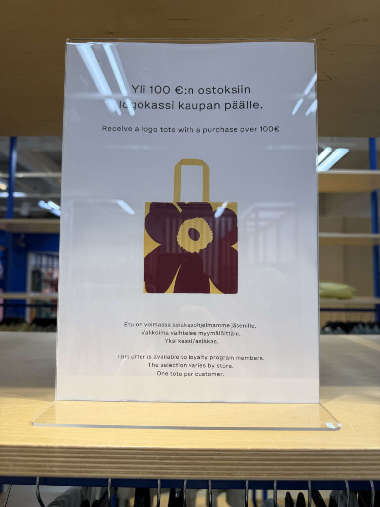 An in-store sign announcing a promotional campaign to receive a Marimekko Unikko pattern tote bag with a purchase of over 100 euros.