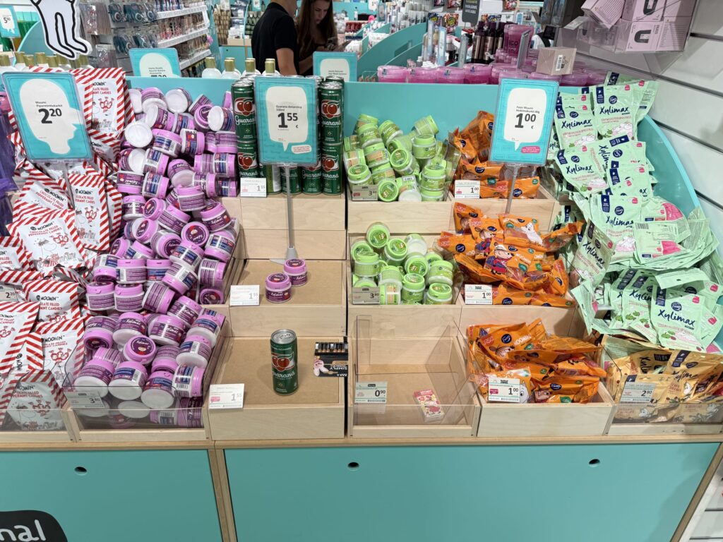 店舗の棚に陳列された様々な種類のムーミンのお菓子。ピンクや緑の容器に入ったキシリトール製品やカラフルな袋入りキャンディーが木箱の中に山積みになっている。