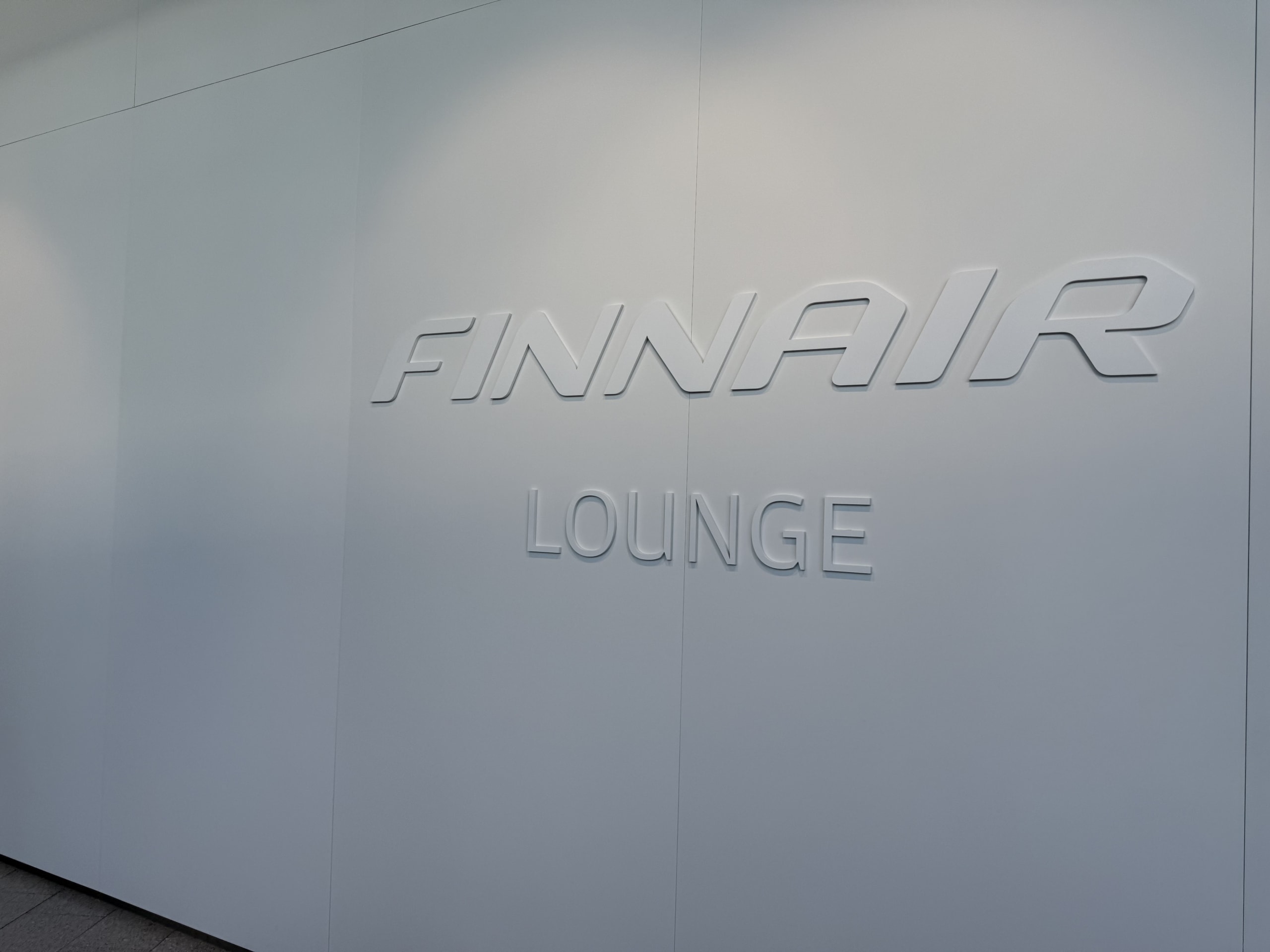 ミニマルなライトグレーの壁に、「FINNAIR LOUNGE」の文字がエンボス加工で施されている様子。