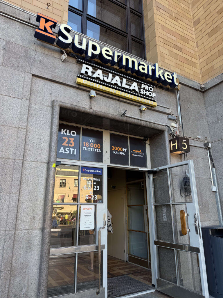 The entrance to a K-Supermarket located in the stone Postitalo (Main Post Office) building in Helsinki, with a large 'K Supermarket' sign above the doorway.