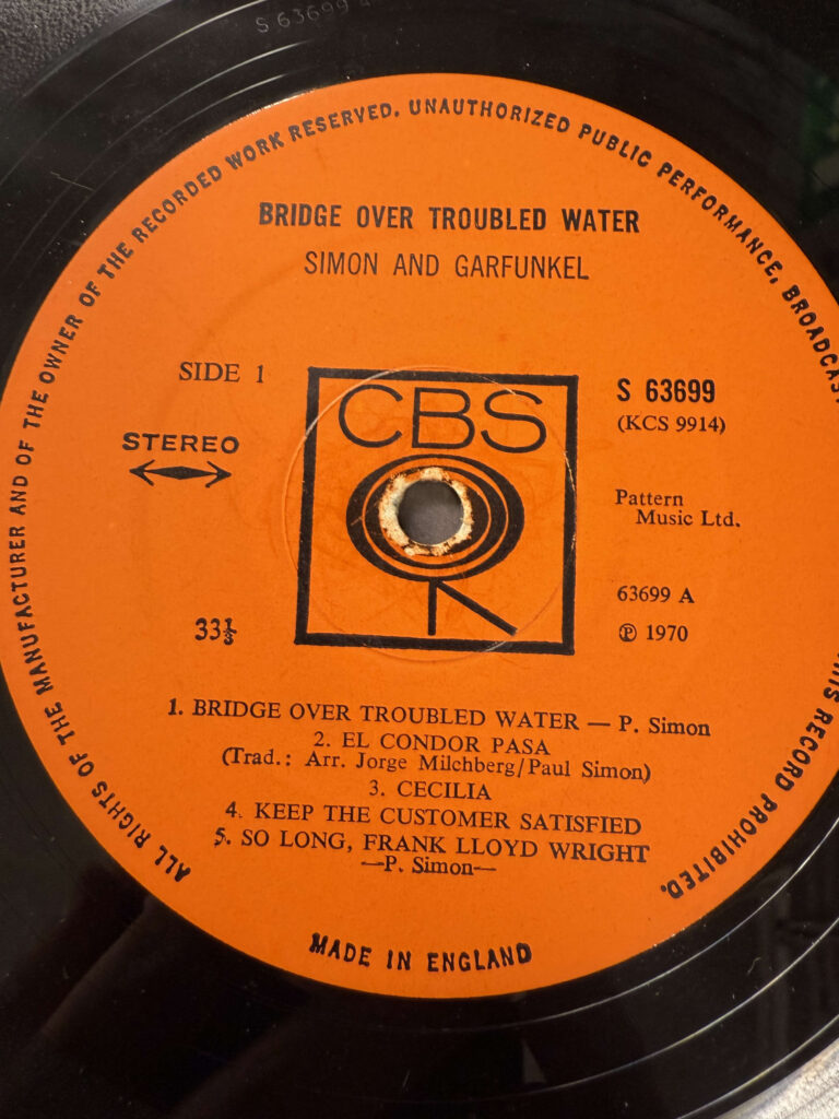 The vinyl record of Simon & Garfunkel's album 'Bridge Over Troubled Water'. It is a European pressing made in England, featuring a vibrant orange CBS label.