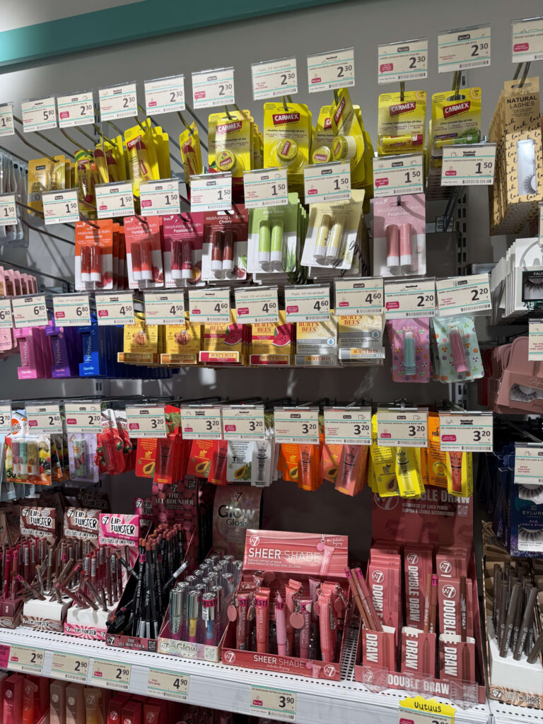 Store shelves fully stocked with a wide variety of lip care products and cosmetics, including brands like Carmex, Burt's Bees, and W7.