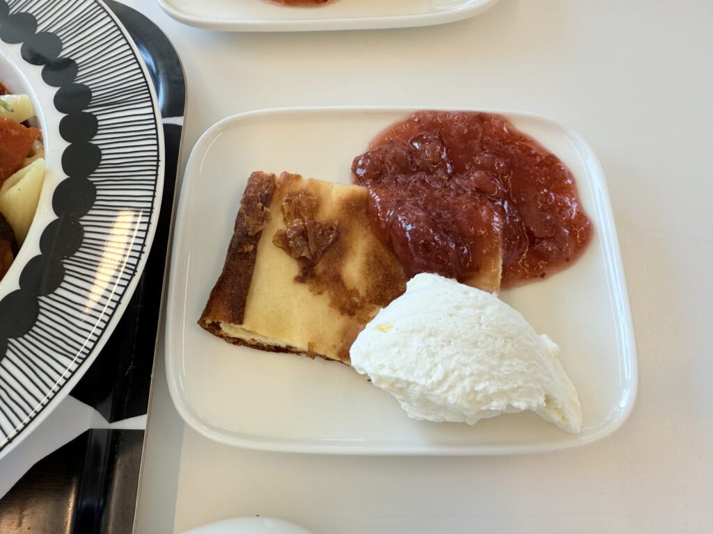 Finnish pancake with strawberry jam and whipped cream on a white plate