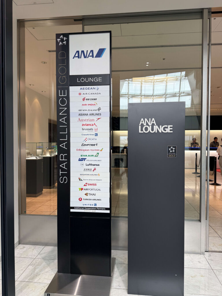 The entrance to the ANA Lounge at Narita Airport. On the left is a tall Star Alliance Gold sign with a list of member airline logos. On the right is a sign for the ANA Lounge.