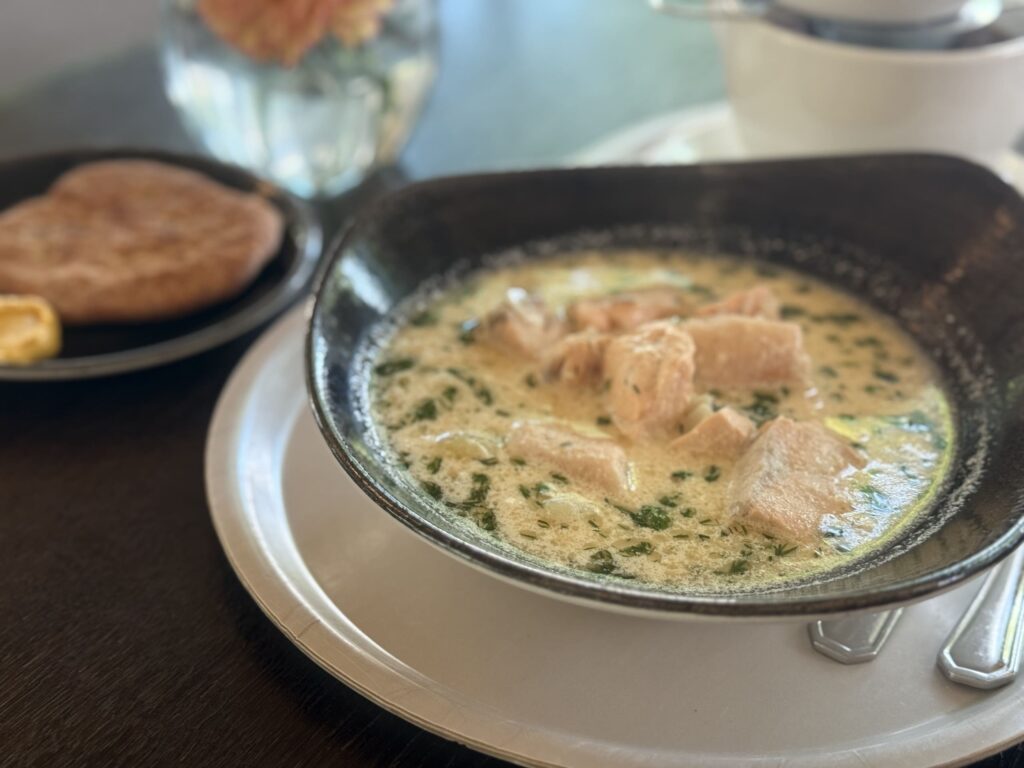 A creamy, hearty salmon soup served in a black bowl, with a side of bread in the background.