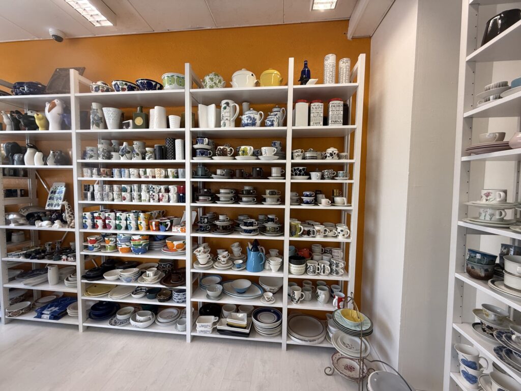 White shelves are packed with Scandinavian-designed vintage cups, saucers, and plates against an orange wall.