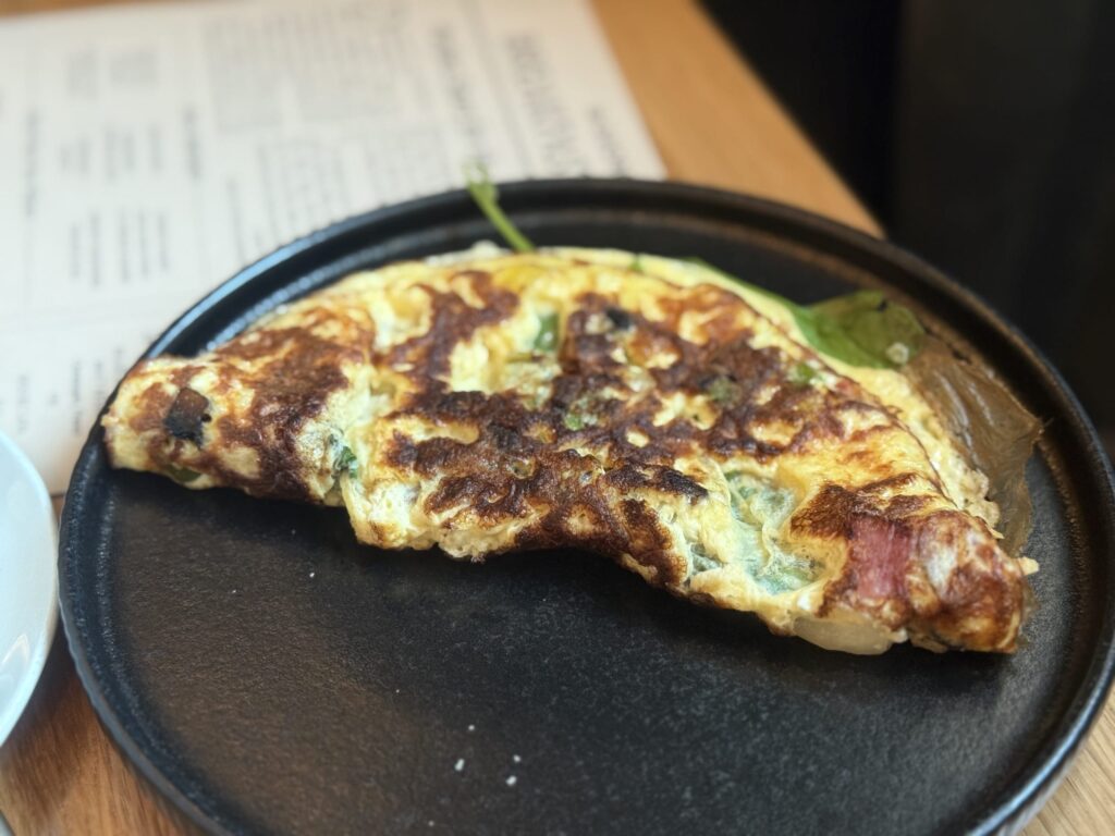 A close-up of a beautifully browned omelette with spinach and ham on a black plate.