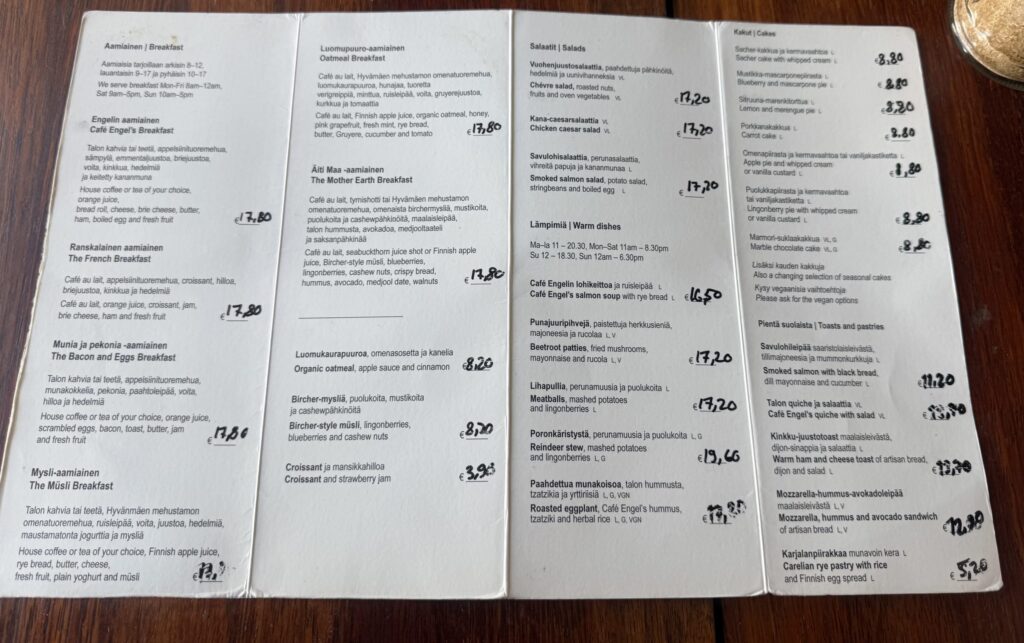 The menu for Café Engel placed on a wooden table. The dish names are written in both Finnish and English.