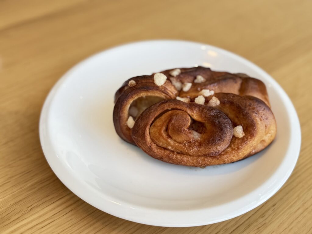 A delicious-looking cinnamon bun sprinkled with pearl sugar, served on a white plate on a wooden table.