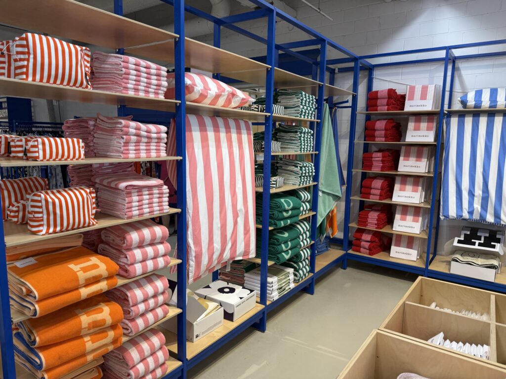 A corner of a store where colorful striped Marimekko towels and pouches in red, pink, green, orange, and blue are displayed on shelves of a blue steel rack.