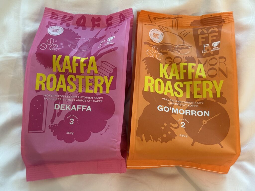 白い布の上に置かれた、KAFFA ROASTERYのコーヒー豆のパッケージ2袋。左側はピンク色のパッケージのデカフェ「DEKAFFA」、右側はオレンジ色のパッケージの「GO'MORRON」。