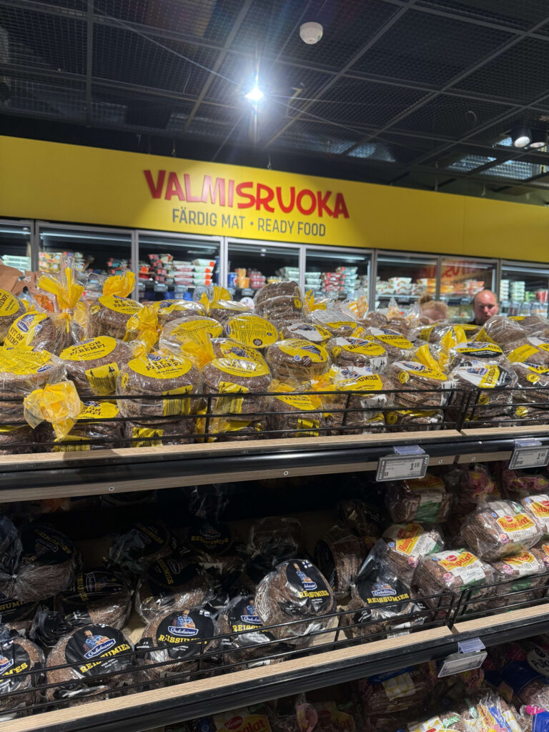 ヴァンター国際空港のスーパーマーケットのパン売り場。棚にはフィンランド名物のライ麦パンがびっしりと並べられており、奥には「VALMISRUOKA(惣菜)」と書かれた黄色い看板が見える。