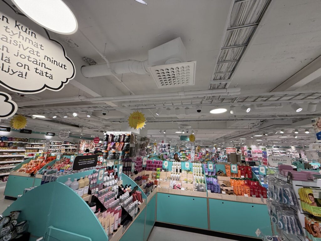 明るい雑貨店の店内。ターコイズ色の棚に化粧品や日用品が所狭しと並べられている様子。