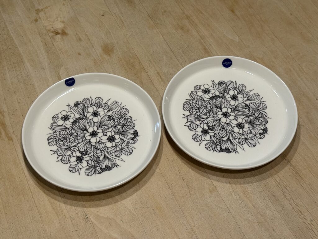 木製のテーブルの上に並べられた2枚の白いお皿。中央には黒い線でクロッカスの花が繊細に描かれており、縁にはARABIAの青いロゴシールが貼られている。