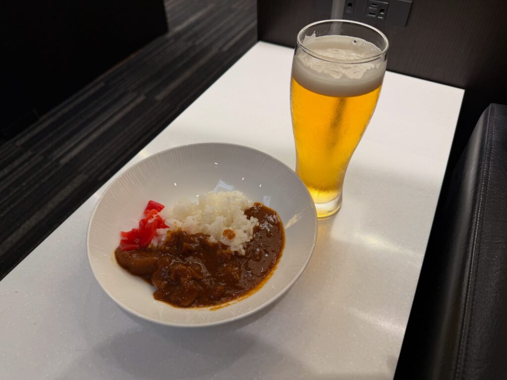 白いテーブルの上に置かれた、福神漬けが添えられたカレーライスとグラスに注がれたビールのセット。