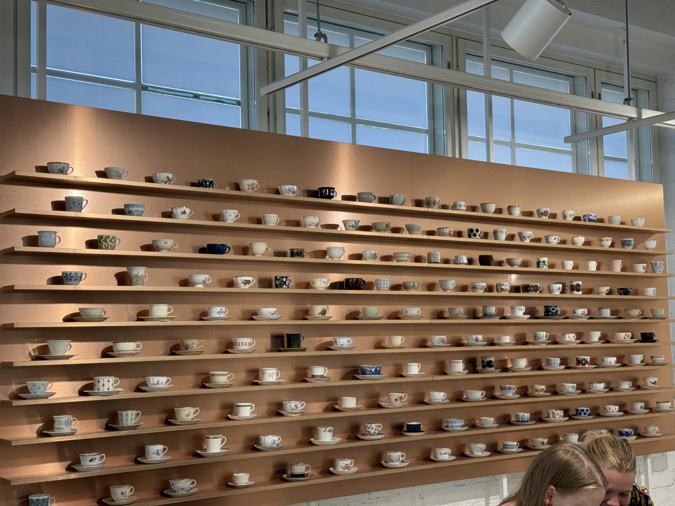 A view of a copper-colored wall with shelves installed all over it, on which various designs of cups and saucers are neatly arranged.