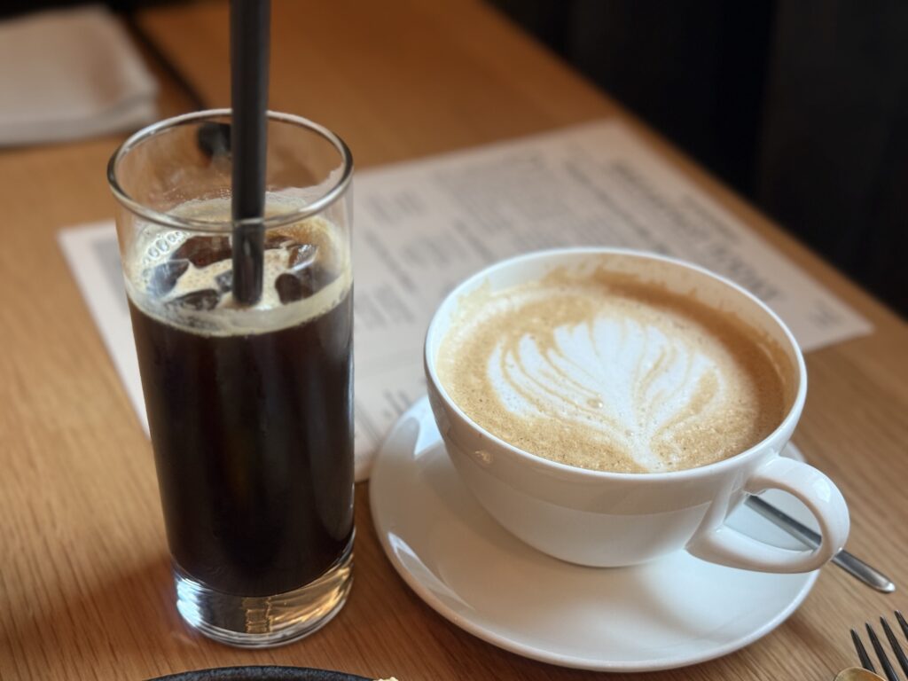 木製のテーブルの上に置かれた、グラス入りのアイスコーヒーと、ラテアートが施された白いカップのカフェラテ。