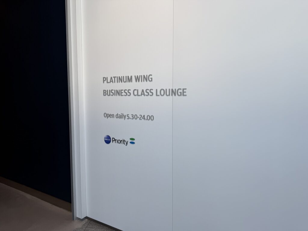 白い壁に「PLATINUM WING BUSINESS CLASS LOUNGE」と書かれた空港ラウンジの入り口。営業時間は「Open daily 5.30-24.00」と表示されている。