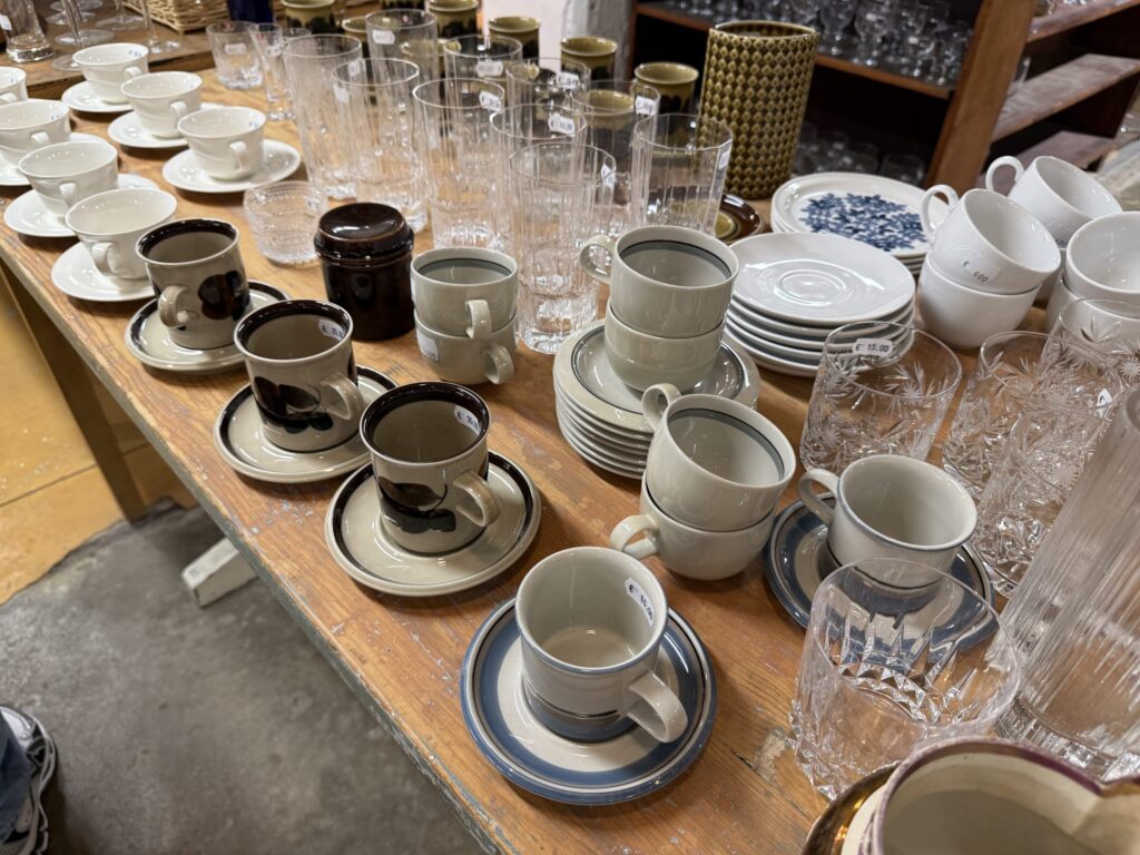 A variety of vintage cups, saucers, and glasses arranged on a wooden table at a secondhand shop in Helsinki.