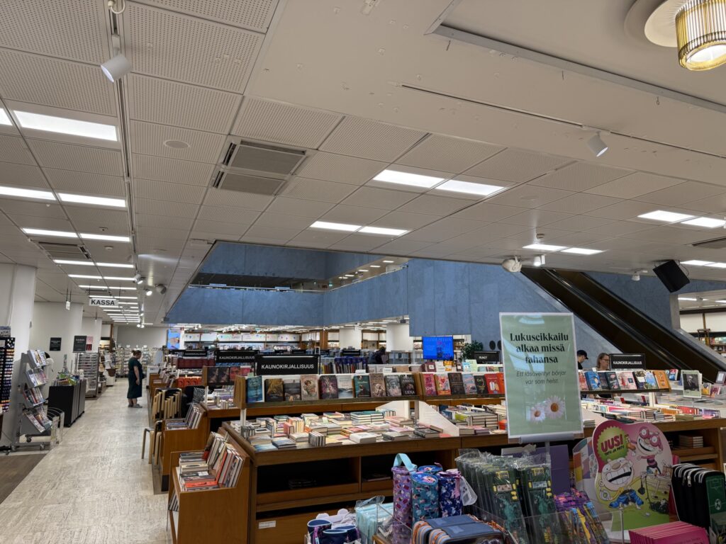 ヘルシンキのアカデミア書店の1階。中央にある吹き抜けの周りに、たくさんの本が並べられた木製の書棚や陳列台が置かれ、数人の客が店内を歩いている。