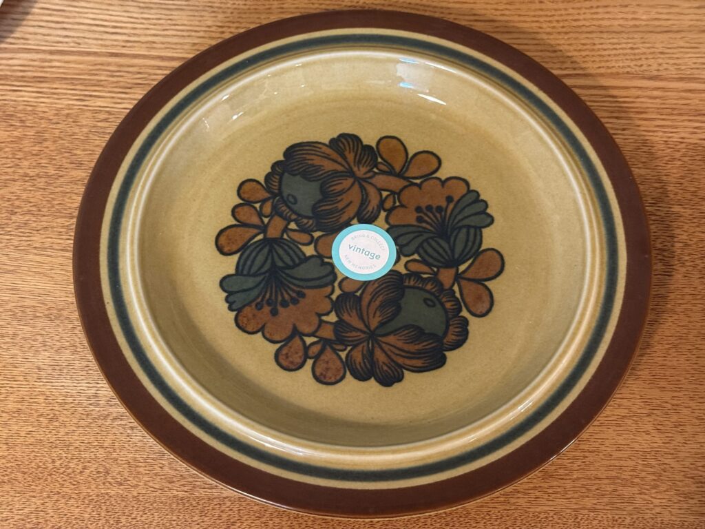 An earth-toned vintage plate with a brown and dark green floral pattern, placed on a wood-grain table.