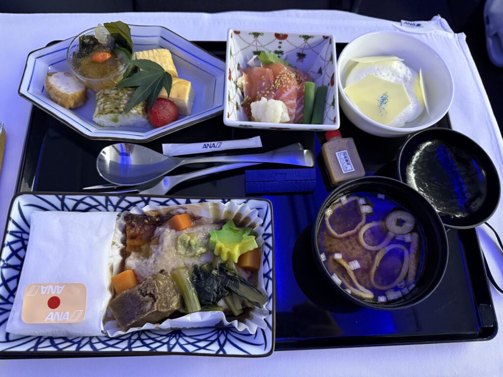 ANAビジネスクラスの機内食。黒いお盆の上に、煮物、刺身、卵焼きなどの和食の小鉢と味噌汁が並べられている。