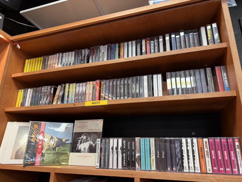 A collection of what appears to be cassette tapes from Finnish artists, packed tightly onto wooden shelves.