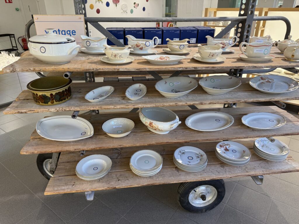 Various pieces of Arabia vintage tableware, including a soup tureen, gravy boats, and plates, displayed on the shelves of a wooden cart.