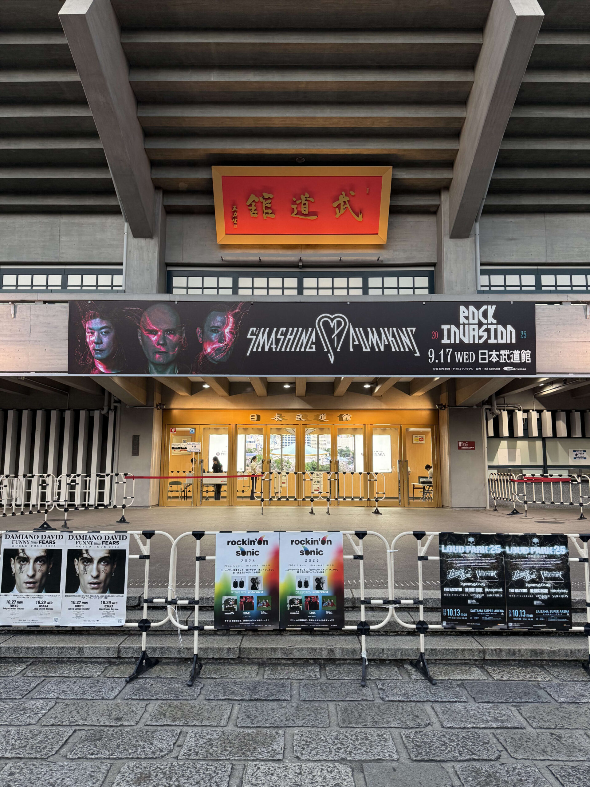 日本武道館の正面玄関。入り口の上にはスマッシング・パンプキンズのコンサート「ROCK INVASION 25」の大きなバナーが掲げられ、手前のバリケードには他のコンサートのポスターが貼られている。