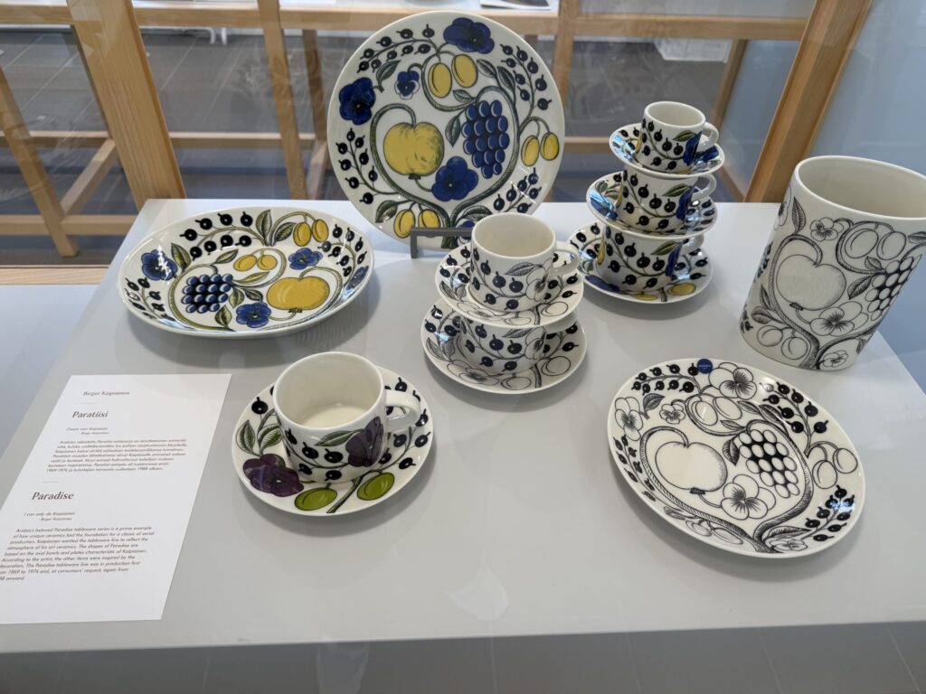 A collection of Arabia's Paratiisi series tableware displayed on a table, featuring both the vibrant color version and the classic black and white version of plates, cups, saucers, and bowls.