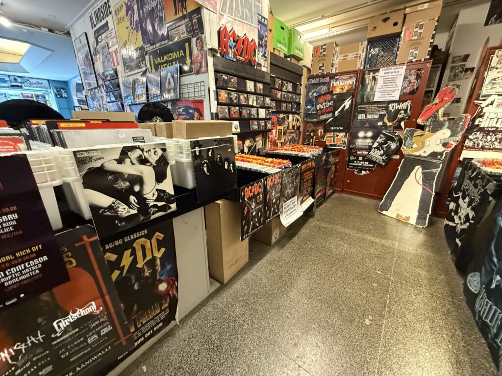 The interior of a record store specializing in heavy metal and hard rock, with walls covered in band posters and bins full of vinyl records.