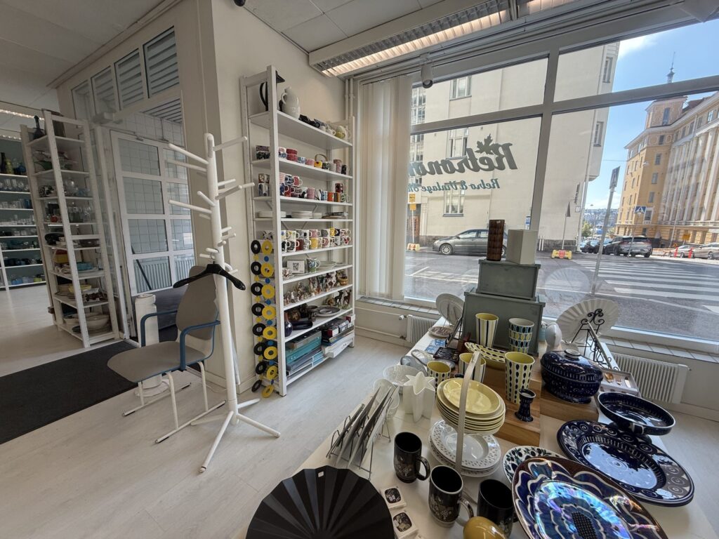 大きな窓から明るい光が差し込むヴィンテージショップの店内。白い棚やテーブルに、色とりどりの陶器やガラス製品が並べられている。