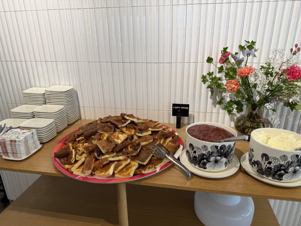 Buffet table with a large platter of Finnish pancakes, jam, cream, plates, and flowers.