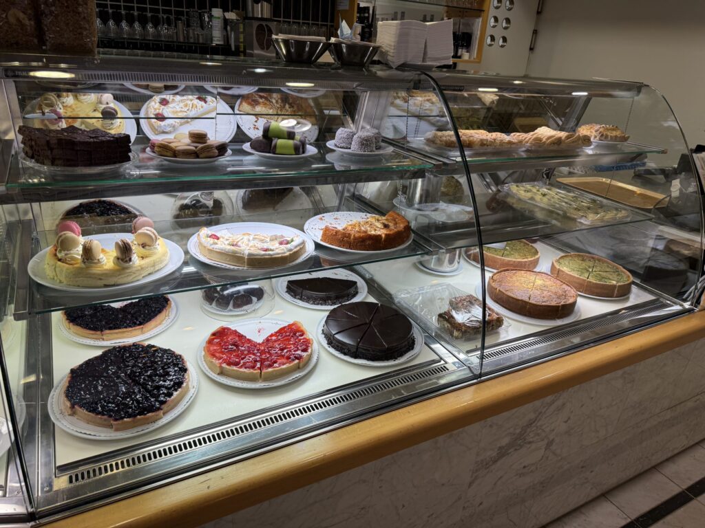 カフェのガラス製ショーケースに、色とりどりのケーキ、タルト、キッシュが何種類も並んでいる様子。
