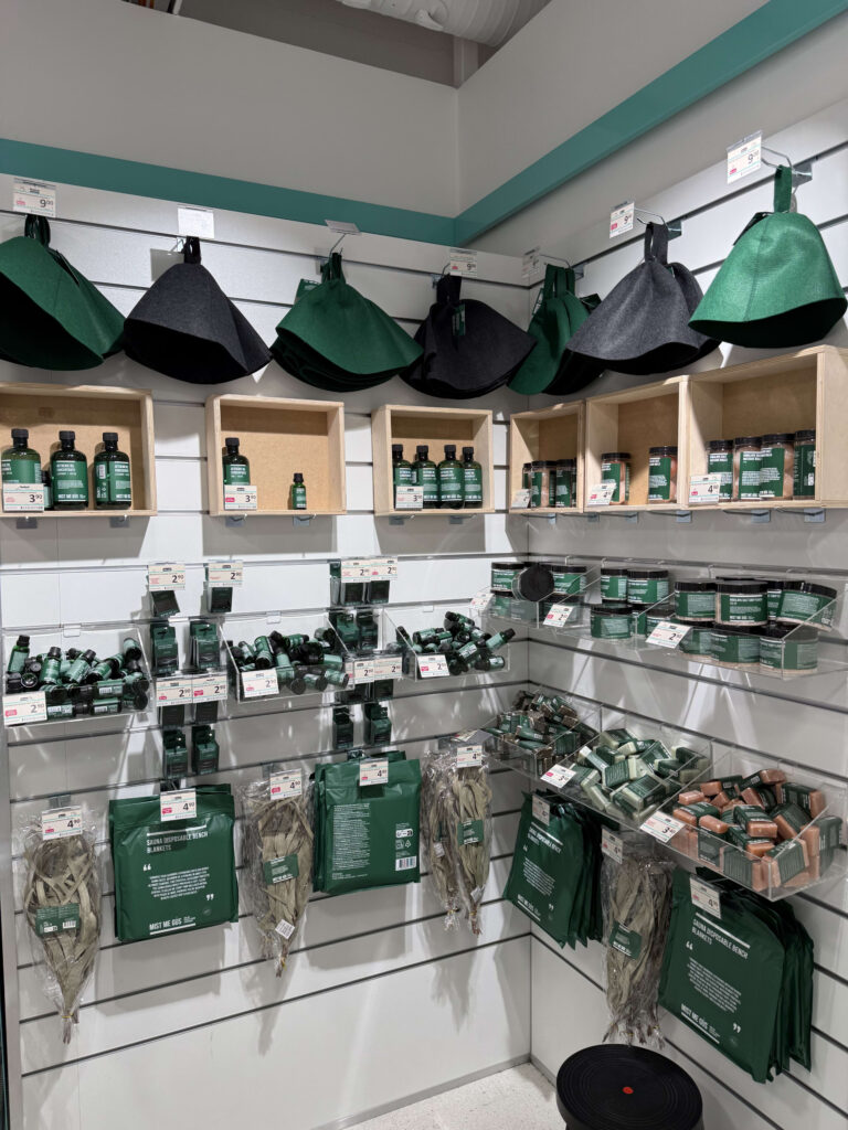 デパートのサウナグッズ売り場。棚に緑と黒のサウナハット、アロマオイル、ソープ、ヴィヒタなどが陳列されている。