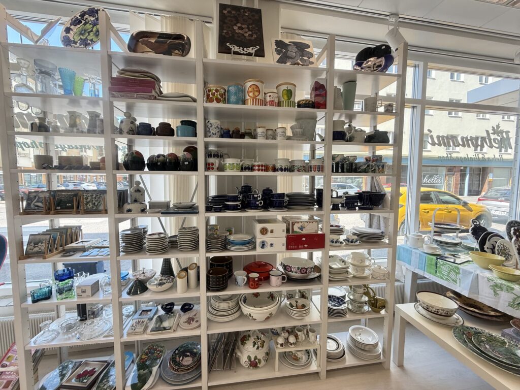 A bright shop interior with tall white shelves packed with vintage Arabia tableware and glassware.
