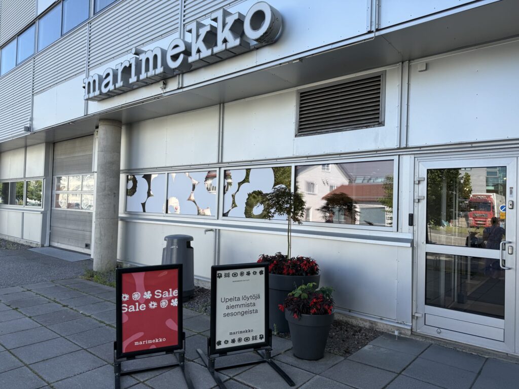 The exterior of the Marimekko outlet store. A red sign announcing a sale stands in front of the modern building's entrance.