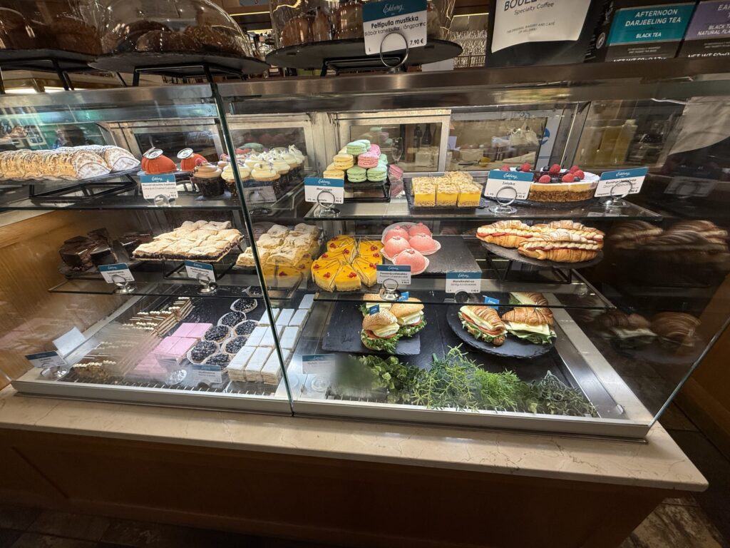 A variety of colorful cakes, sandwiches, macarons, and other pastries are beautifully displayed in a glass showcase at a cafe.
