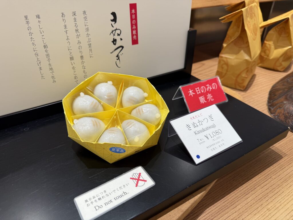 黒いお盆の上に置かれた、黄色い六角形の箱に入った和菓子「きぬかづき」。本日のみ販売という赤い札と、値段が書かれた白い札が添えられている。