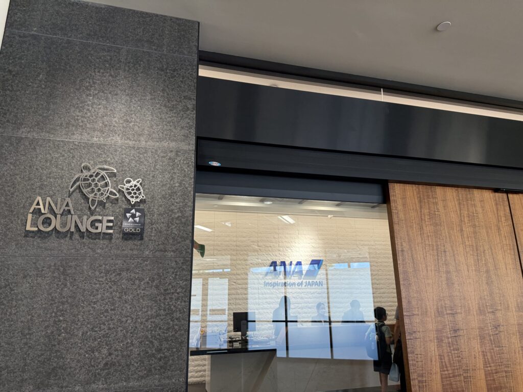 The entrance to the ANA Lounge at Daniel K. Inouye International Airport. A stone-style wall features the silver text 'ANA LOUNGE' and a Hawaiian-style honu (sea turtle) logo.