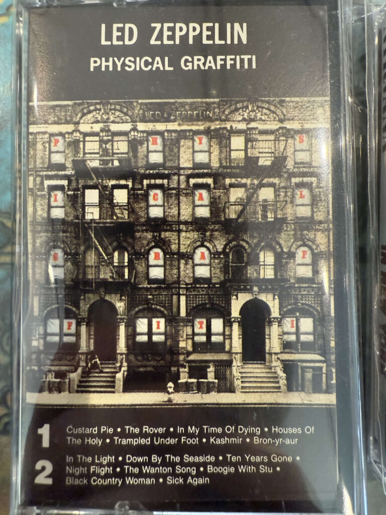 A close-up of the Led Zeppelin album 'Physical Graffiti' on a cassette tape, sealed in its clear plastic case.