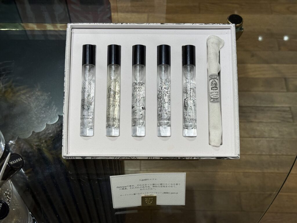 ガラスのテーブルの上に置かれた、diptyqueのフレグランスディスカバリーセット。白い箱の中に、イラストが描かれた5本のミニ香水ボトルと布製のポーチが並んでいる。