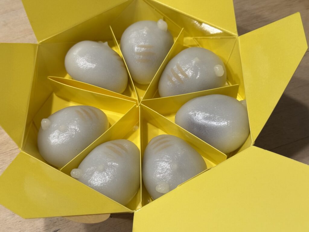 An open, bright yellow, star-shaped box containing seven translucent, rabbit-shaped Japanese dumplings, each in its own triangular compartment.